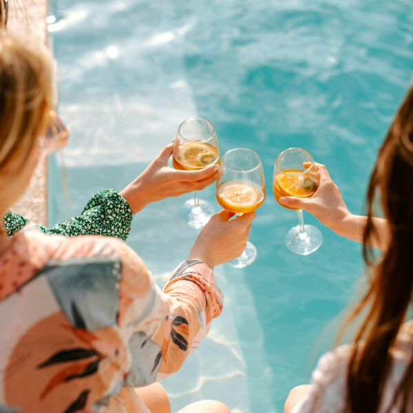 Friends toasting cocktails together on edge of outdoor pool.