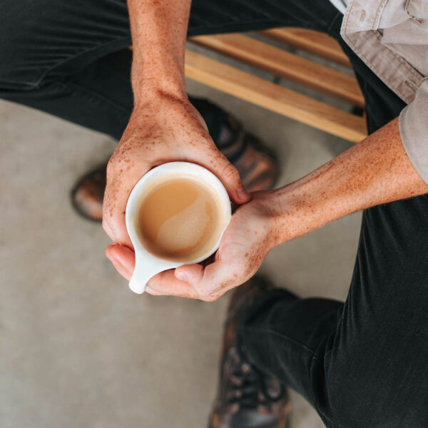 Person seated on bench enjoying latte in mug.