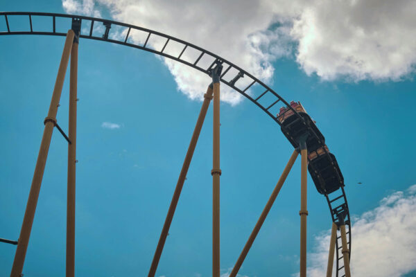 People riding on roller coaster under bright summer skies.